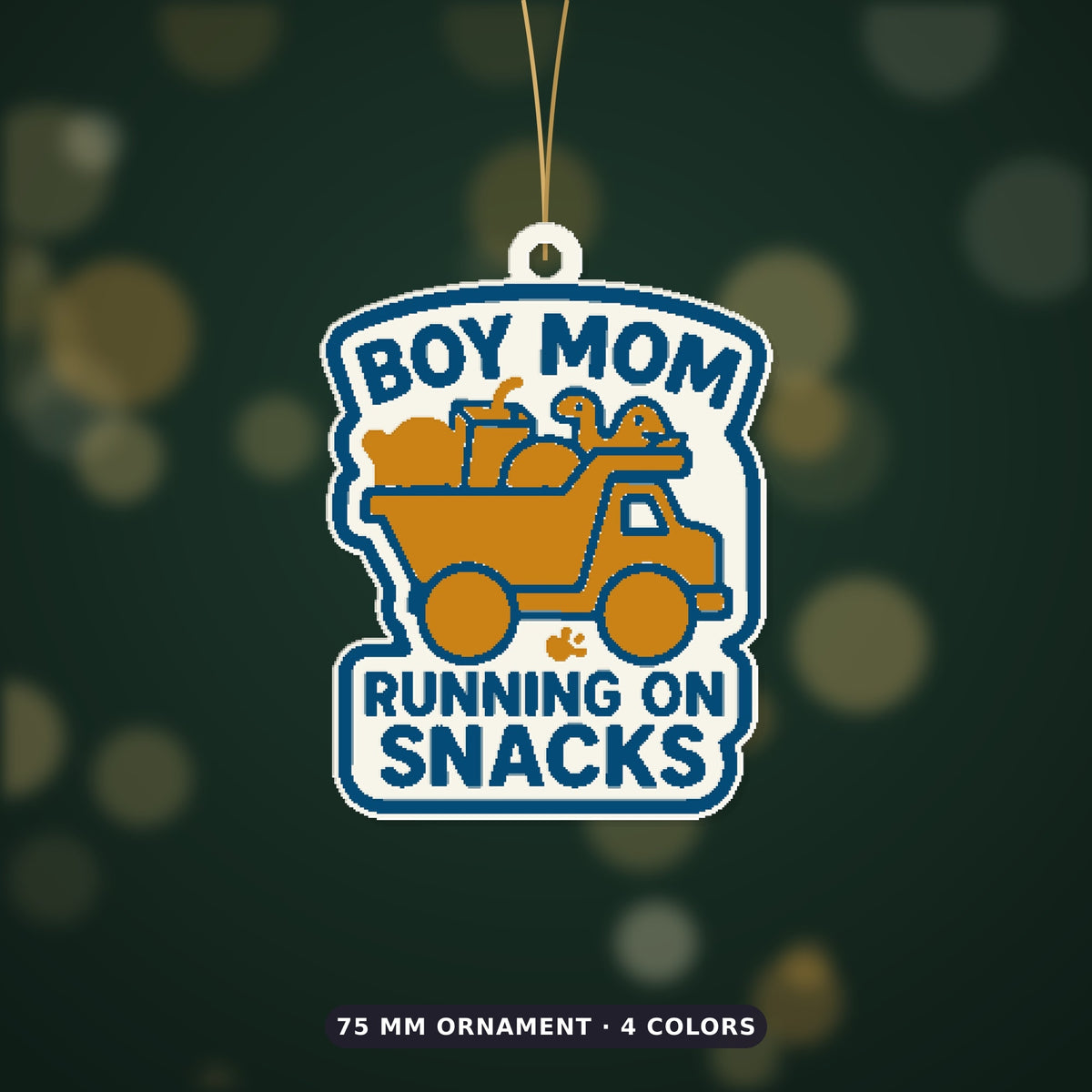 Round-cornered ornament with a blue border and the text Boy Mom Running On Snacks above an orange toy dump truck carrying a teddy bear, a juice cup, a ball and a dinosaur, hanging on a dark green bokeh background.