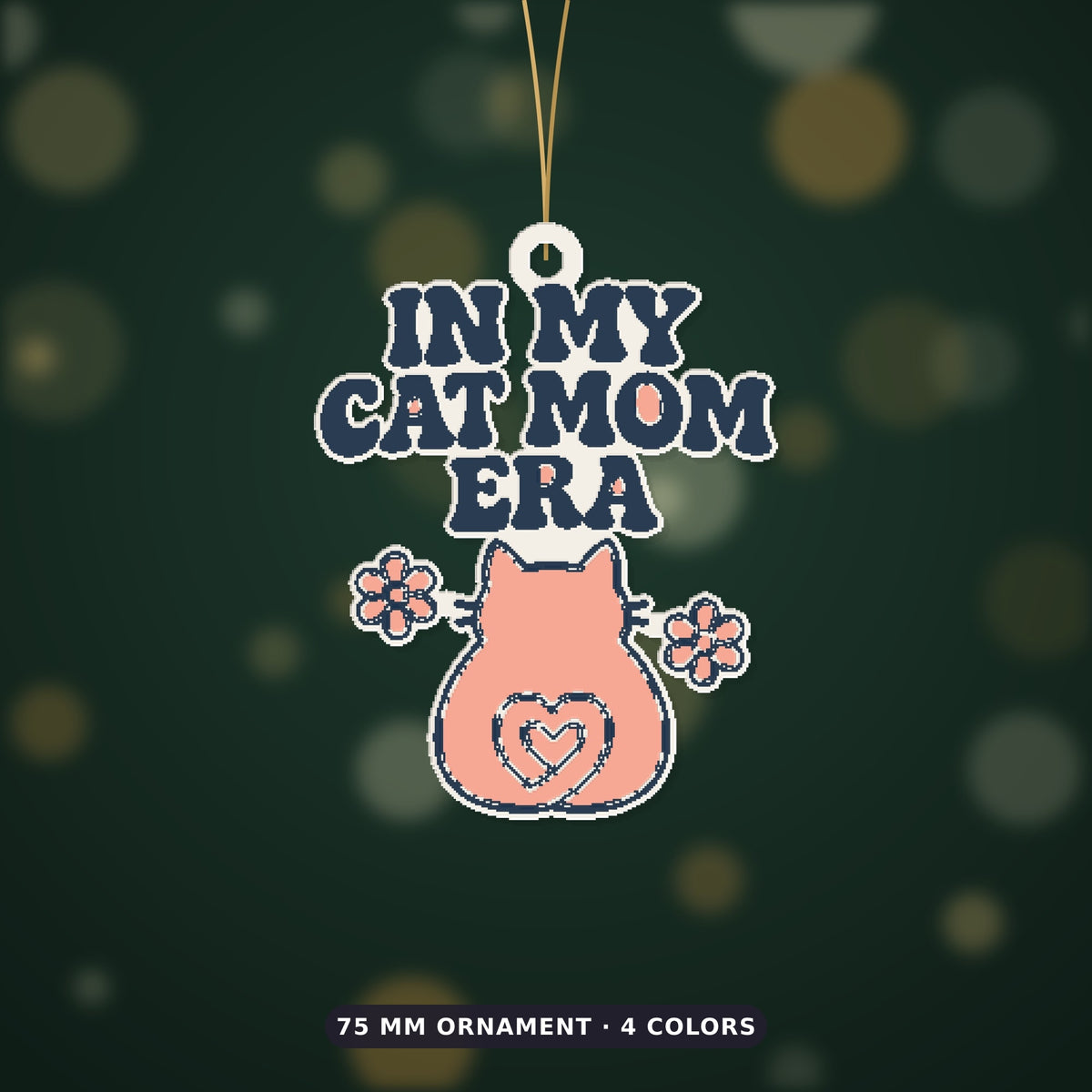 Pixel-style ornament with navy retro wavy text "In My Cat Mom Era" above a pink cat seen from behind with a heart-shaped tail and two flowers, on a dark green bokeh background labeled 75 mm ornament, 4 colors.