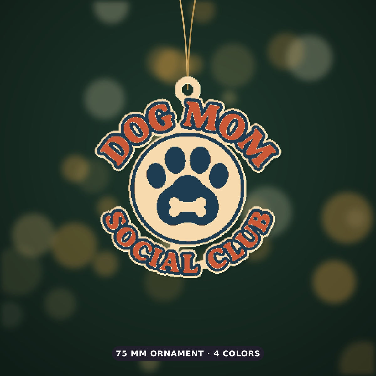Round Dog Mom Social Club ornament with an orange retro lettering border and a navy paw print with a bone on a cream badge, hanging on a gold string against a dark green background with golden bokeh lights.