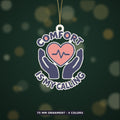 Ornament-shaped design with a pink heart and heartbeat line held by two navy hands, surrounded by the words Comfort Is My Calling on a dark green background labeled 75 mm ornament, 4 colors.