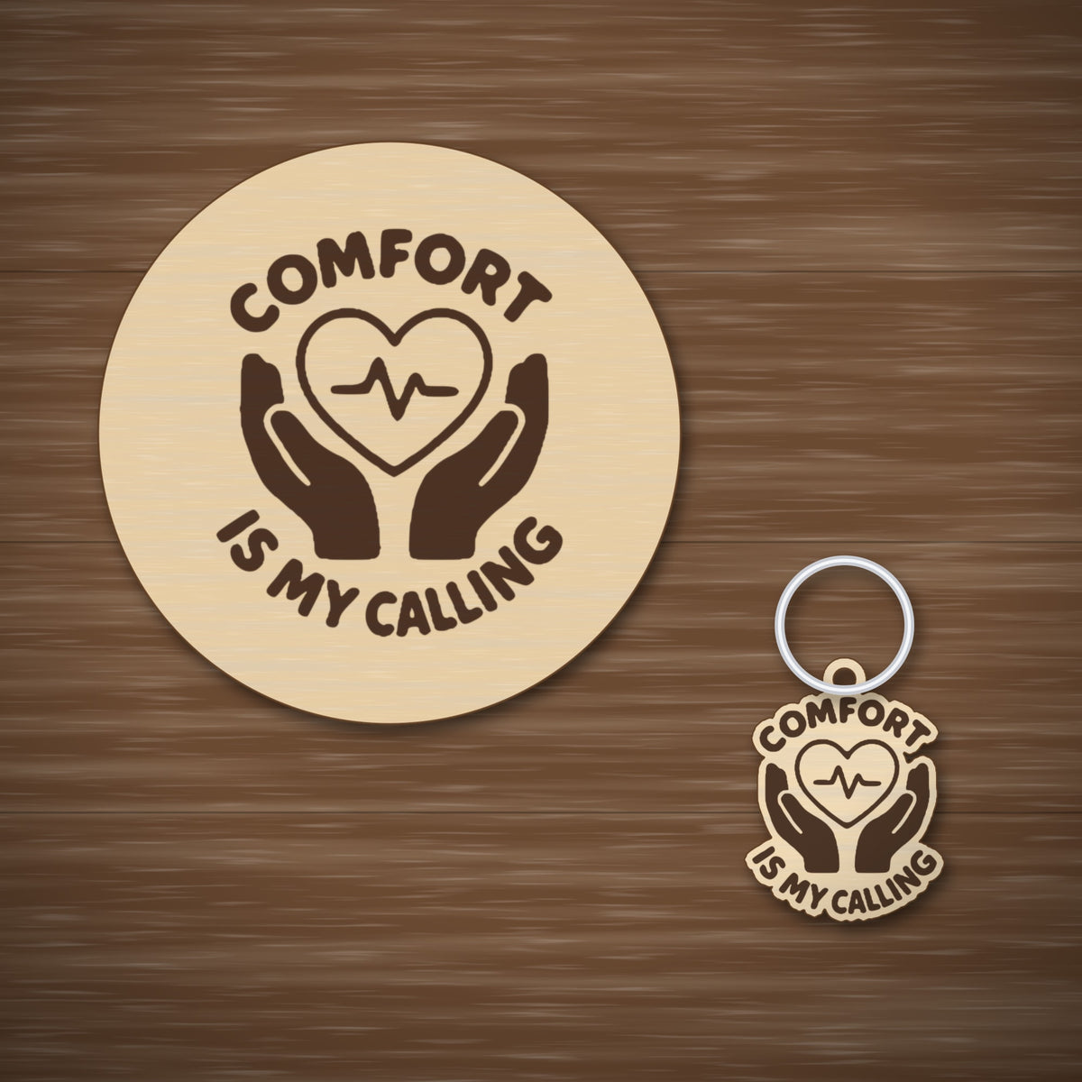 Round-edged wooden ornament with an engraved heart and pulse line held by two hands, with the words Comfort Is My Calling, hanging against a dark green blurred light background.
