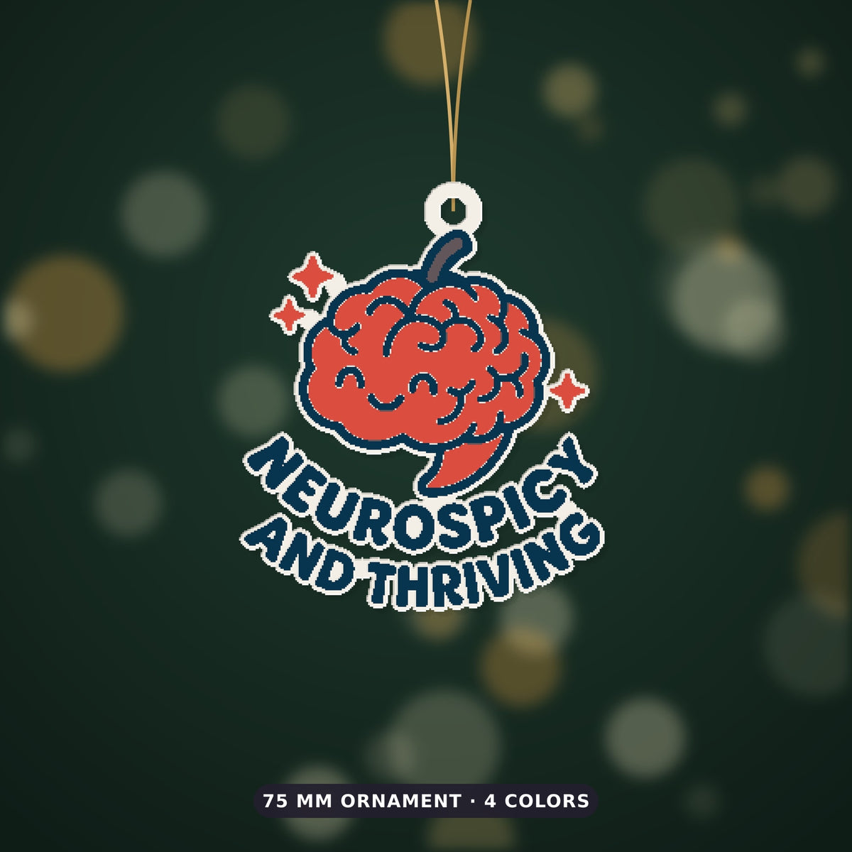 A 75 mm ornament of a smiling red chili-pepper brain with sparkles and the words Neurospicy and Thriving, hanging on a gold cord against a dark green bokeh background.