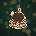 Wooden laser cut ornament with a dark brown engraved brain with a chili stem and the words Neurospicy and Thriving, hanging on a gold string against a green background with soft bokeh lights.