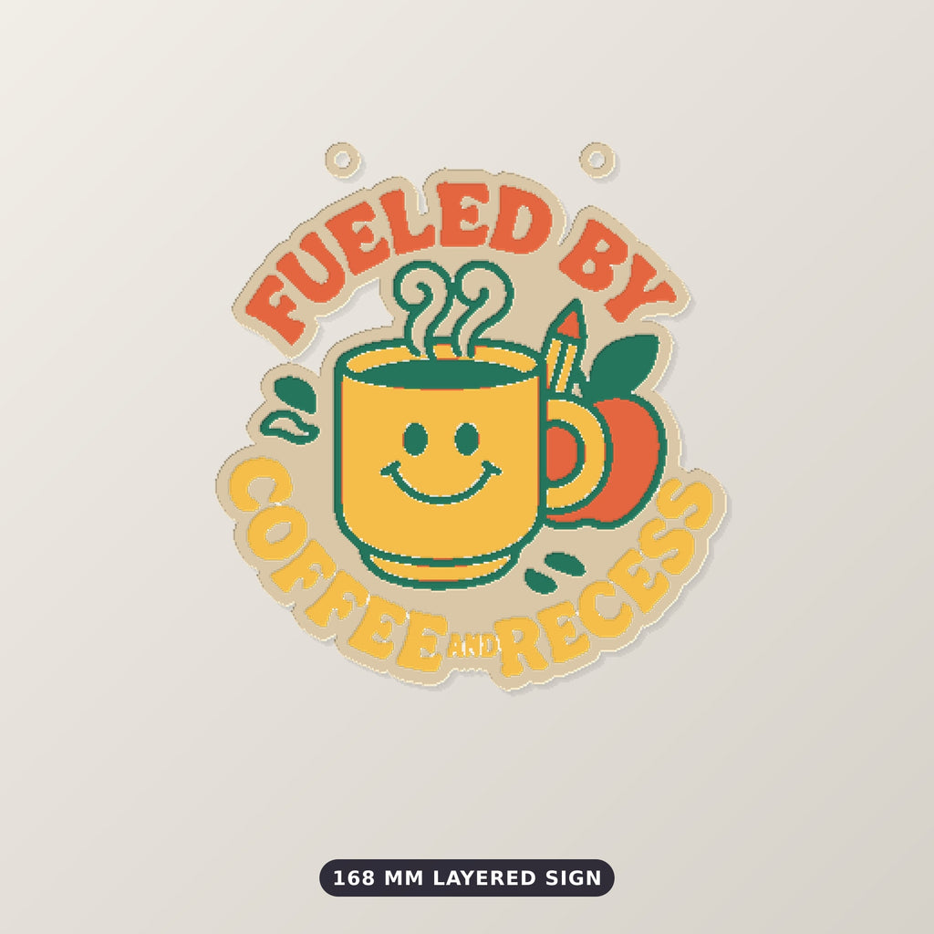 Round ornament with a smiling yellow coffee mug, green steam, an apple and a pencil, surrounded by the text Fueled by Coffee and Recess, on a dark green background with golden bokeh lights.