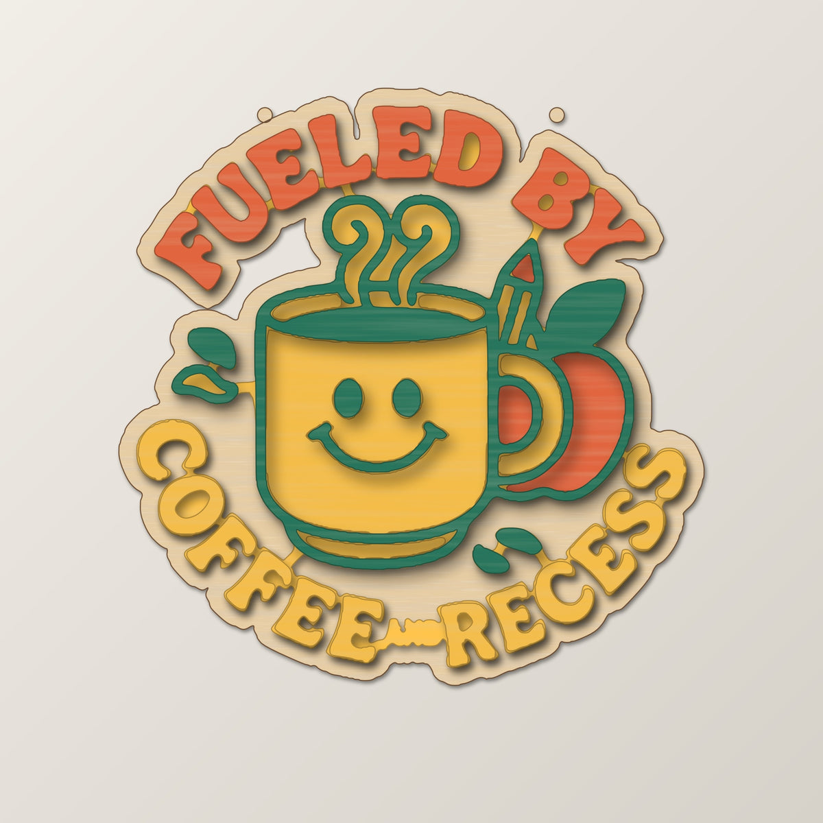 Round wooden laser-engraved ornament with the words Fueled By above a smiling coffee mug, a pencil and an apple, hanging on a thin cord against a dark green background with golden bokeh lights.