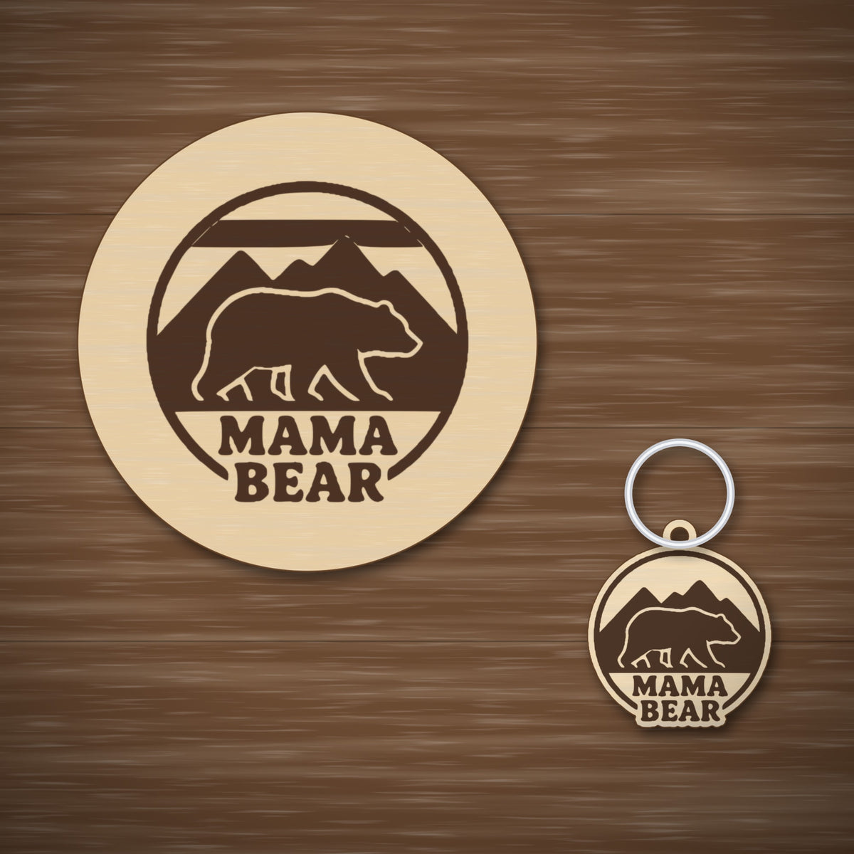 Round wooden laser cut ornament showing a brown bear walking in front of mountains above the words Mama Bear, hanging on a thin cord against a blurred green background with golden lights.
