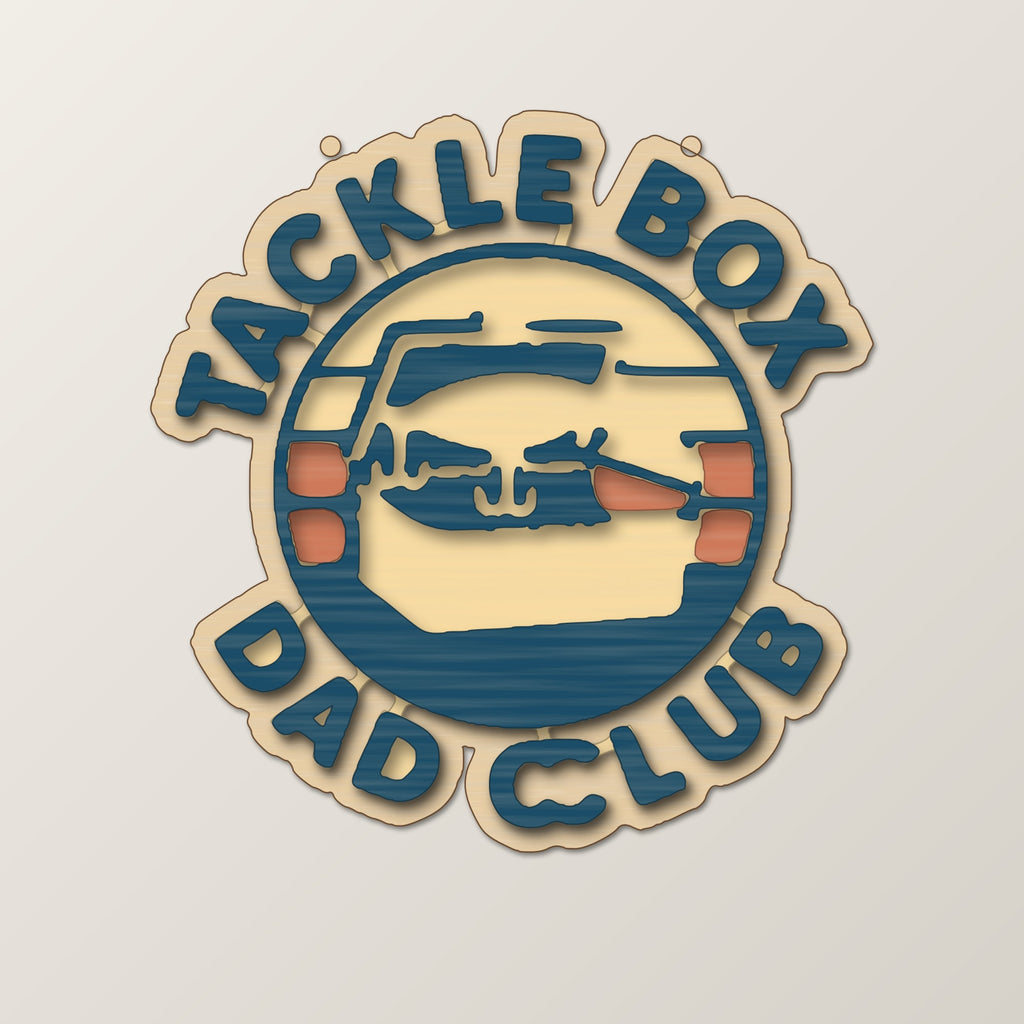 Round wooden laser engraved ornament with a retro tackle box and fishing lure badge and the words Tackle Box Dad Club, hanging on a thin cord against a dark green background with soft golden lights.