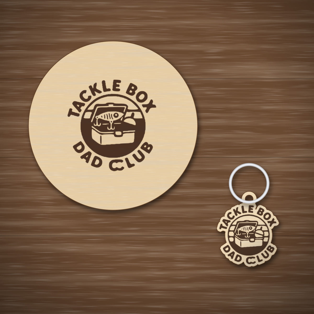 Round wooden laser engraved ornament with a retro tackle box and fishing lure badge and the words Tackle Box Dad Club, hanging on a thin cord against a dark green background with soft golden lights.