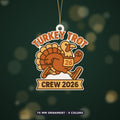 A cartoon turkey in running shoes and a number 26 race bib on a round ornament that reads Turkey Trot at the top and Crew 2026 on a ribbon banner below.