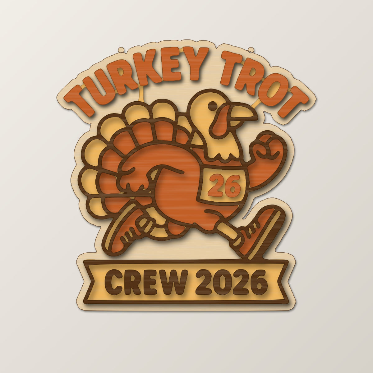 A laser cut wooden ornament showing a cartoon turkey running in a race bib numbered 26, with the words Turkey Trot above and Crew 2026 on a banner below, hanging against a dark green background.