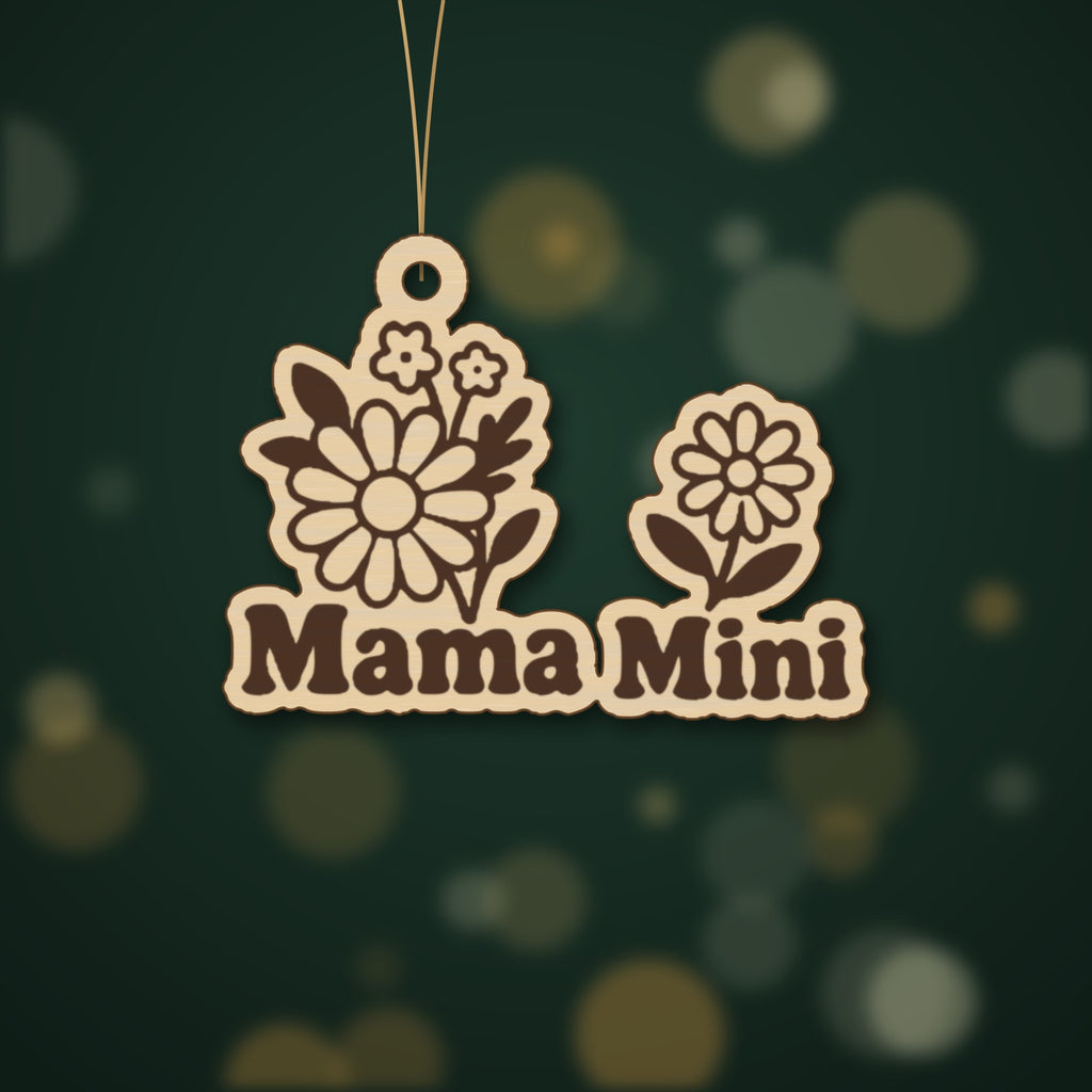 Wooden laser cut ornament with engraved daisy bouquet and single daisy, reading Mama Mini, hanging by a thin cord against a dark green background with golden bokeh lights.