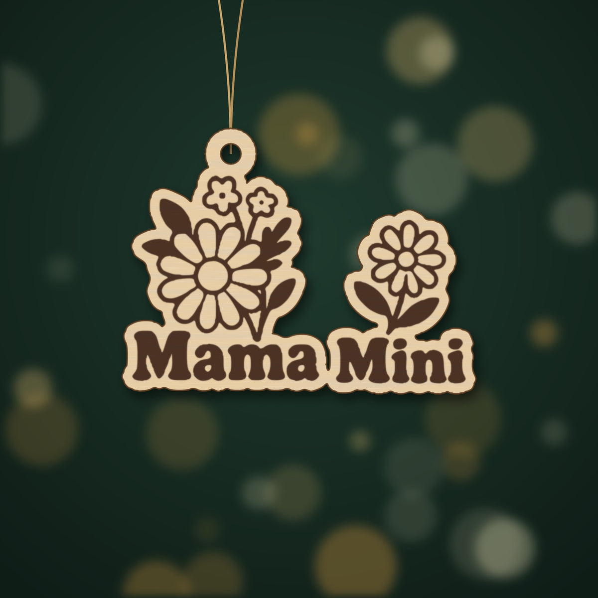 Wooden laser cut ornament with engraved daisy bouquet and single daisy, reading Mama Mini, hanging by a thin cord against a dark green background with golden bokeh lights.